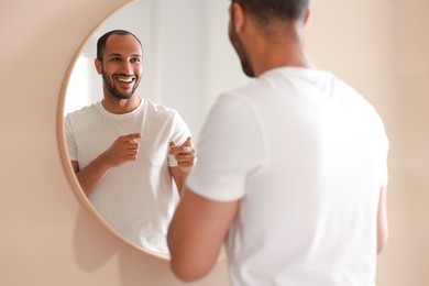 Photo of Smiling man looking at mirror in bathroom, back view