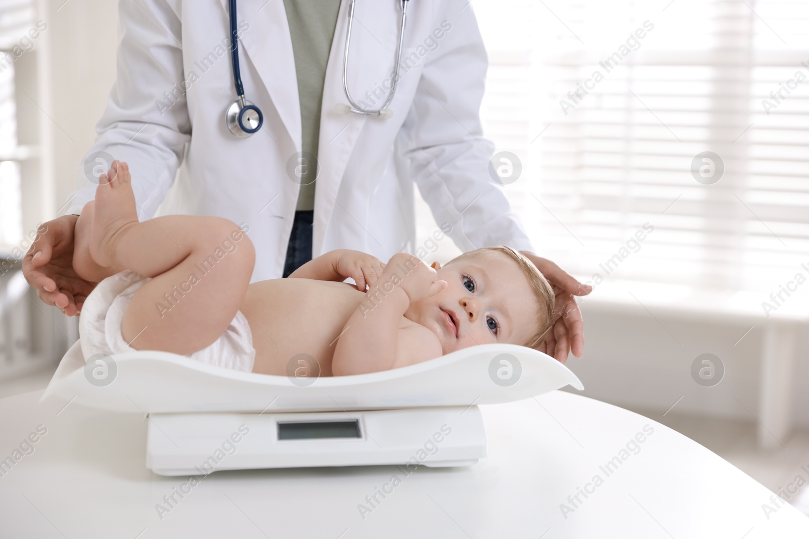 Photo of Pediatrician weighting little child in clinic, closeup. Checking baby's health