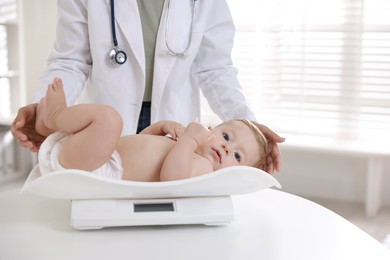 Photo of Pediatrician weighting little child in clinic, closeup. Checking baby's health