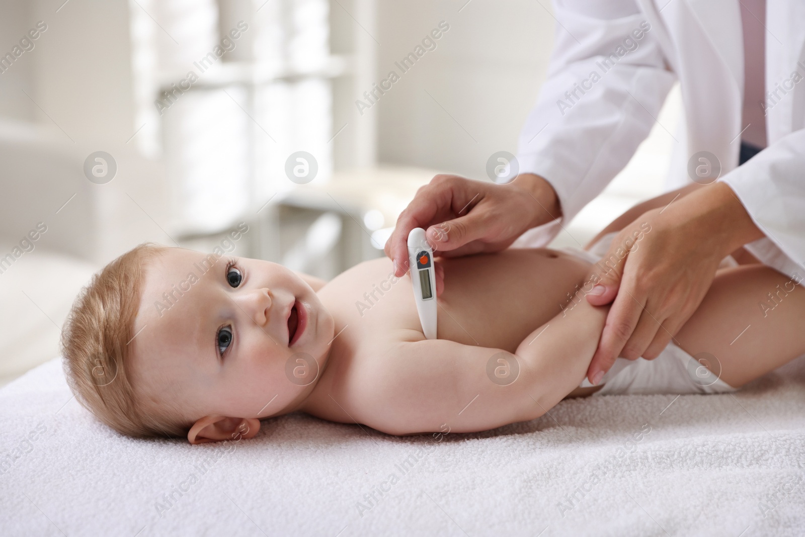 Photo of Pediatrician examining little child with thermometer in clinic, closeup. Checking baby's health