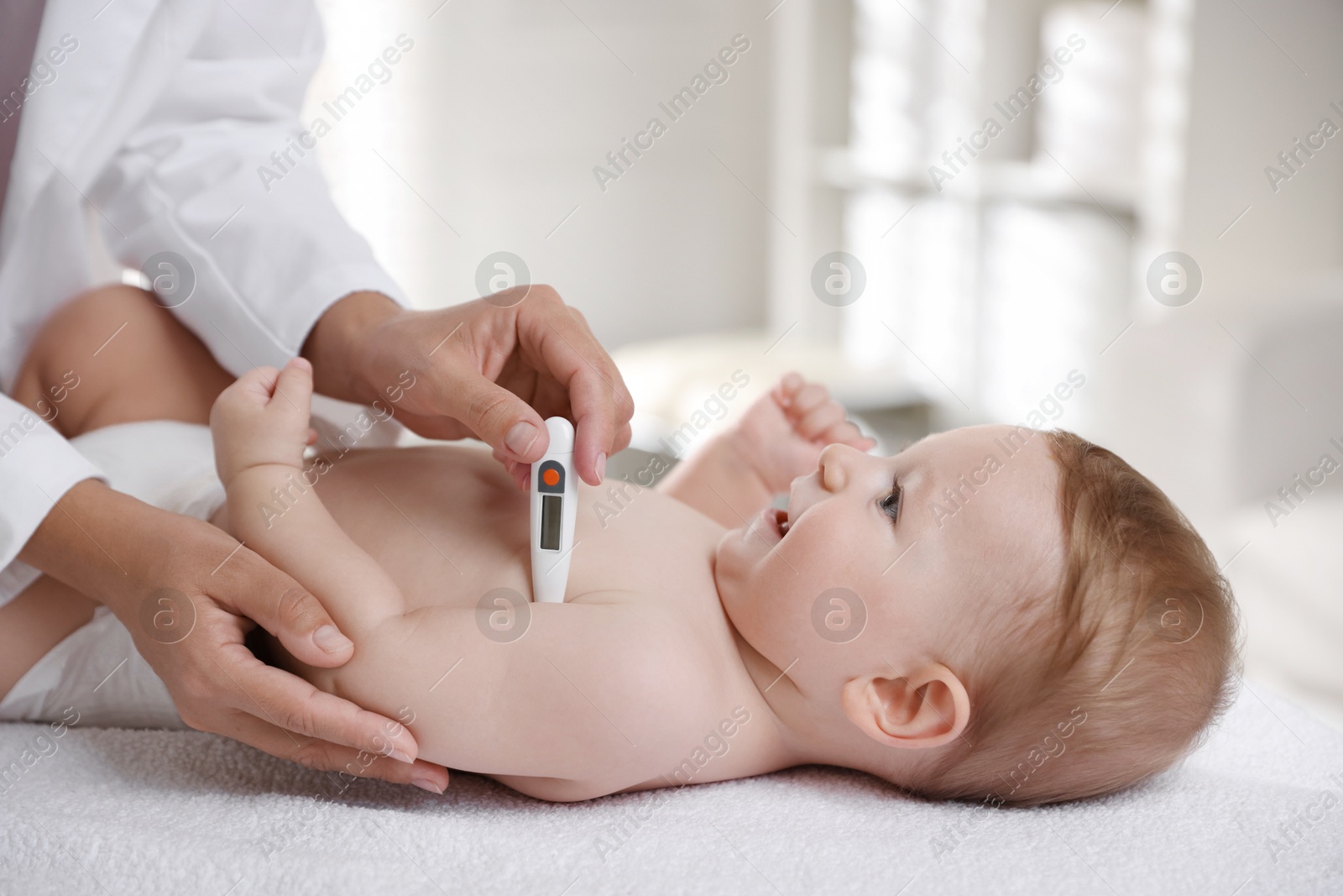 Photo of Pediatrician examining little child with thermometer in clinic, closeup. Checking baby's health