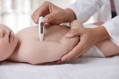 Photo of Pediatrician examining little child with thermometer in clinic, closeup. Checking baby's health