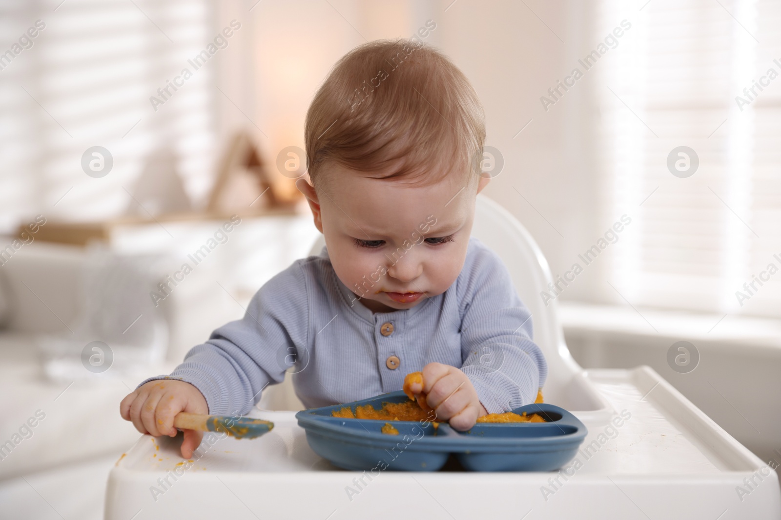 Photo of Cute little baby eating healthy food in high chair indoors