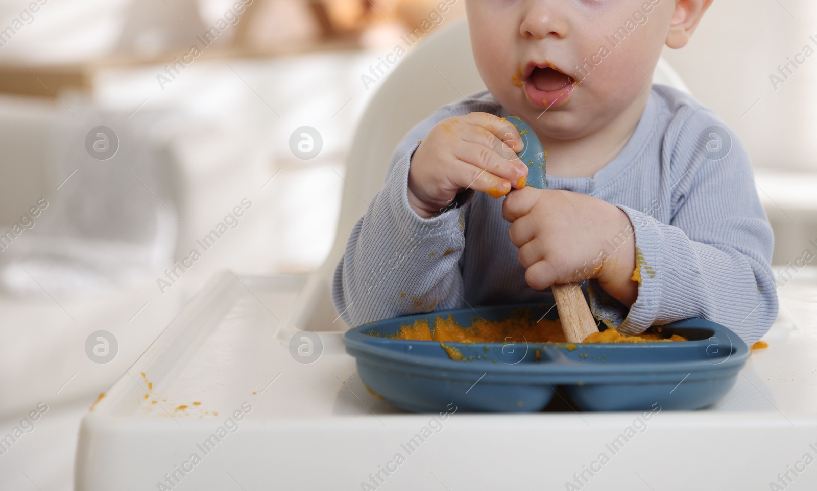 Photo of Cute little baby eating healthy food in high chair indoors, closeup