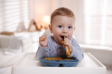 Photo of Cute little baby eating healthy food in high chair indoors