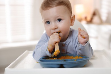 Photo of Cute little baby eating healthy food in high chair indoors