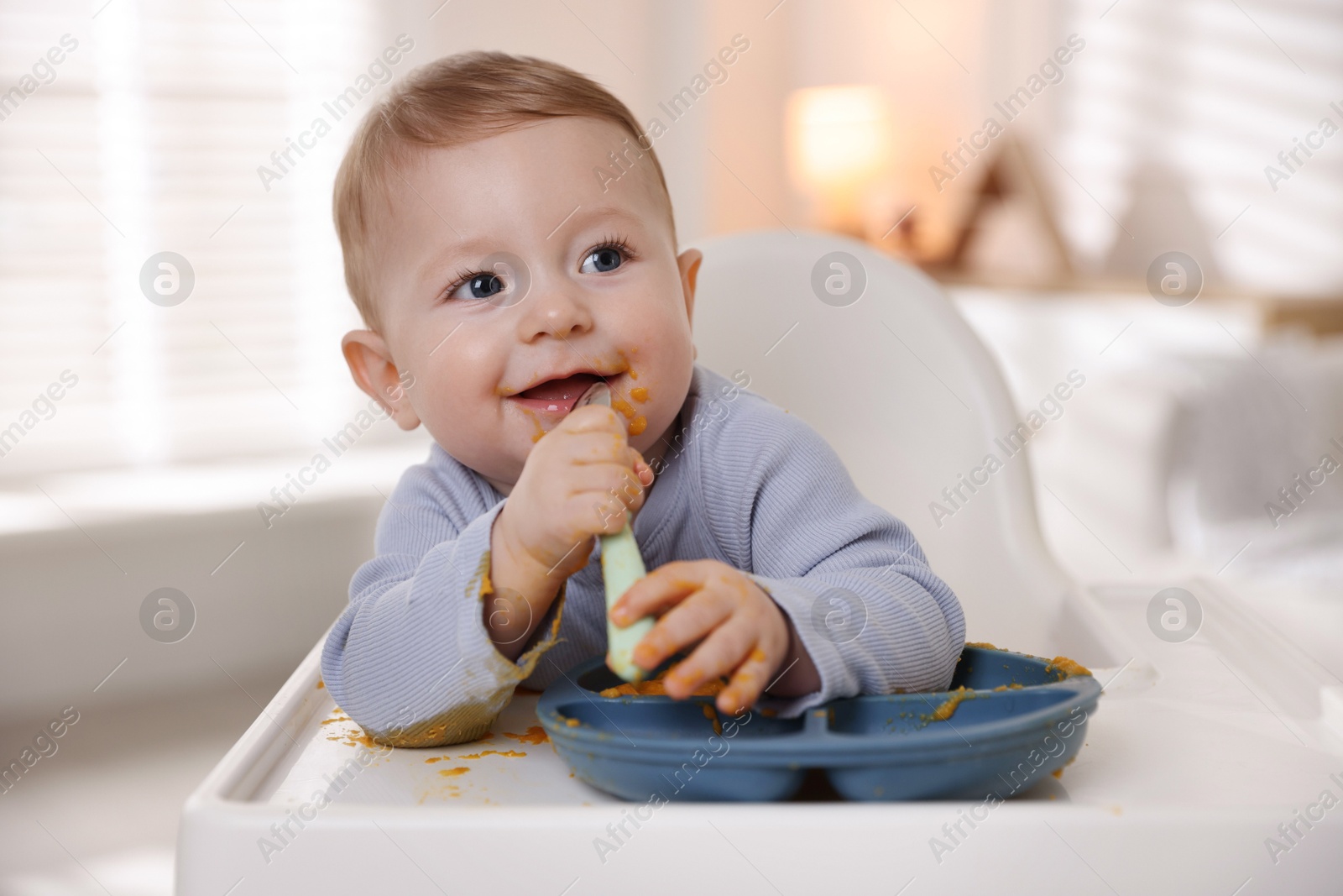 Photo of Cute little baby eating healthy food in high chair indoors