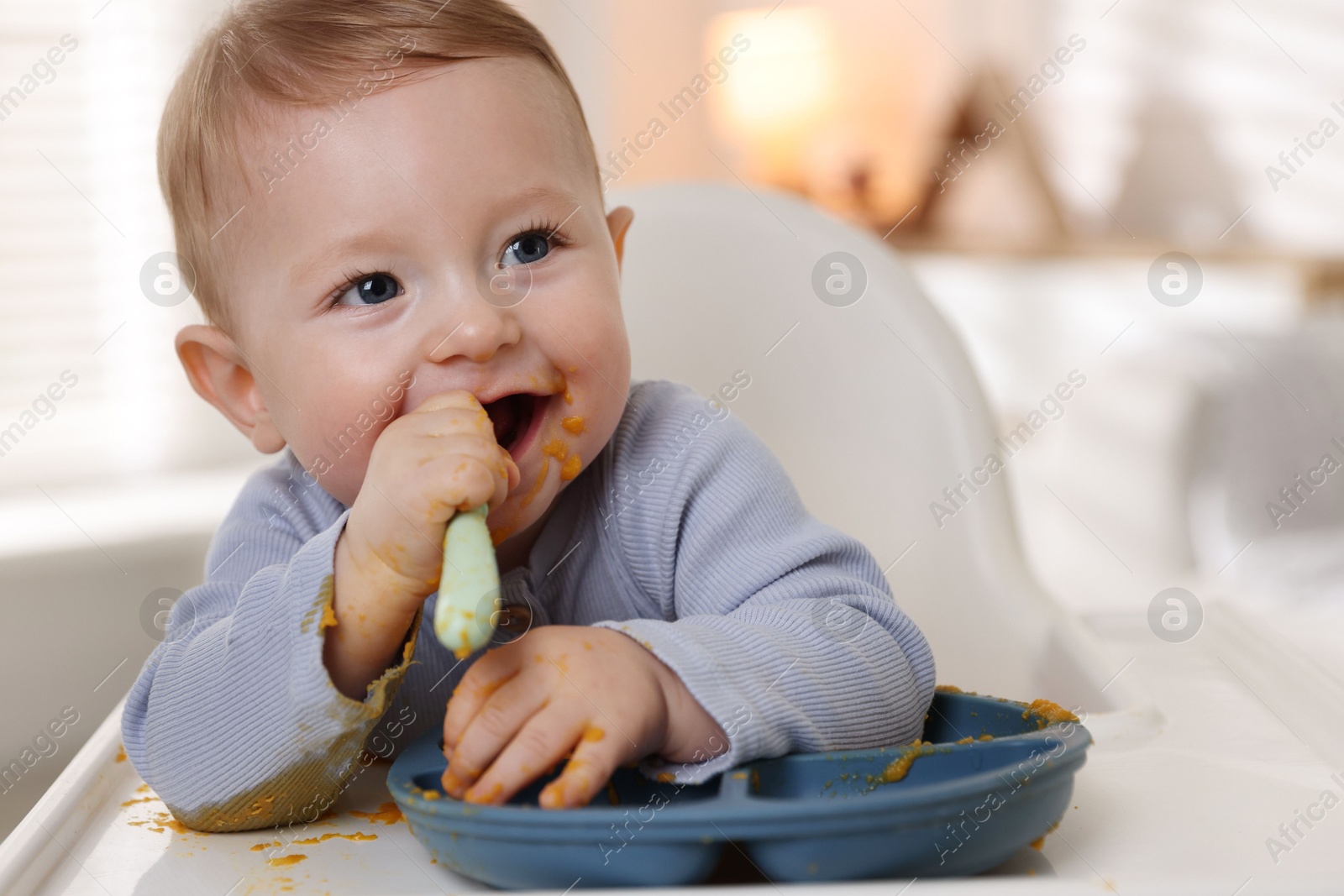 Photo of Cute little baby eating healthy food in high chair indoors