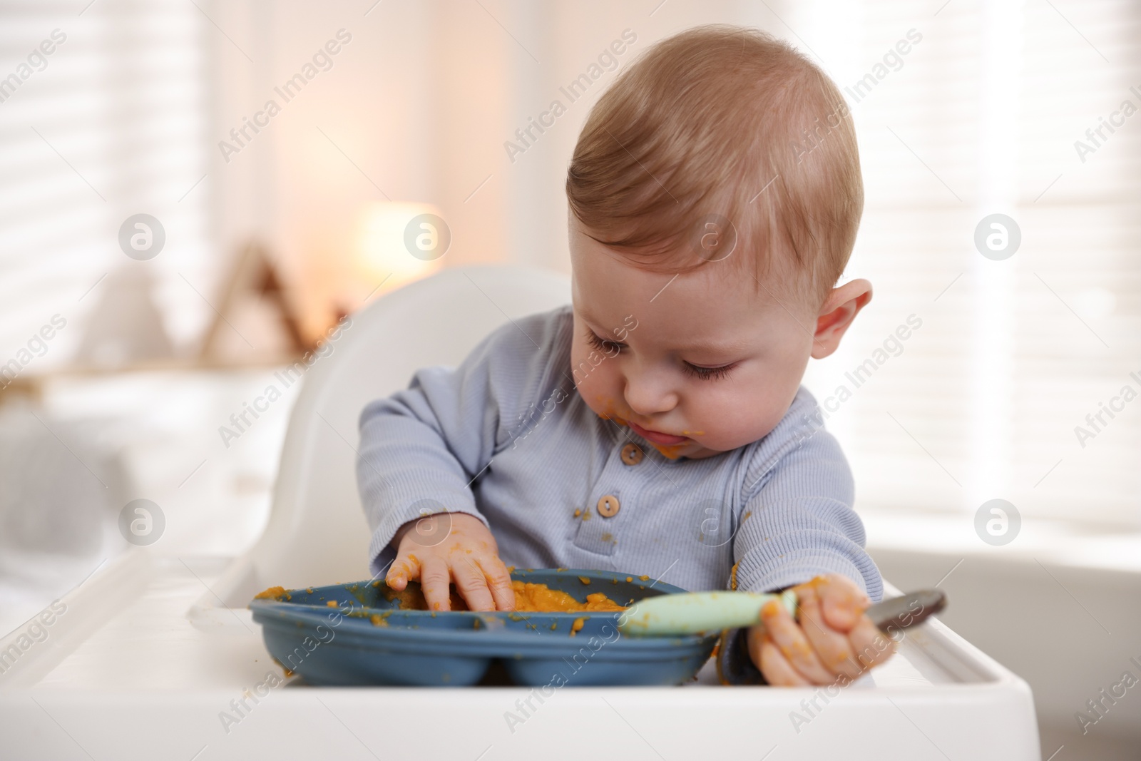 Photo of Cute little baby eating healthy food in high chair indoors