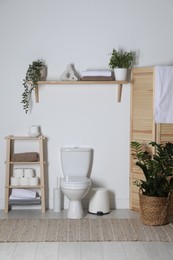 Photo of Folding screen, toilet bowl and houseplants in restroom. Interior design