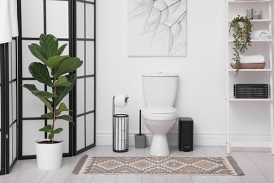 Photo of Stylish restroom interior with folding screen, toilet bowl and houseplant