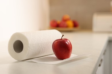 Photo of Roll of paper towels and red apple on white countertop in kitchen, closeup. Space for text