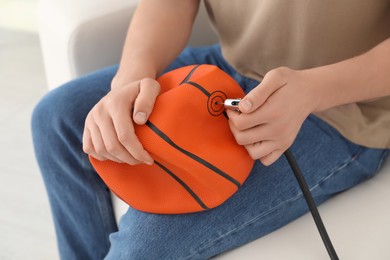 Photo of Man inflating basketball ball with air compressor indoors, closeup