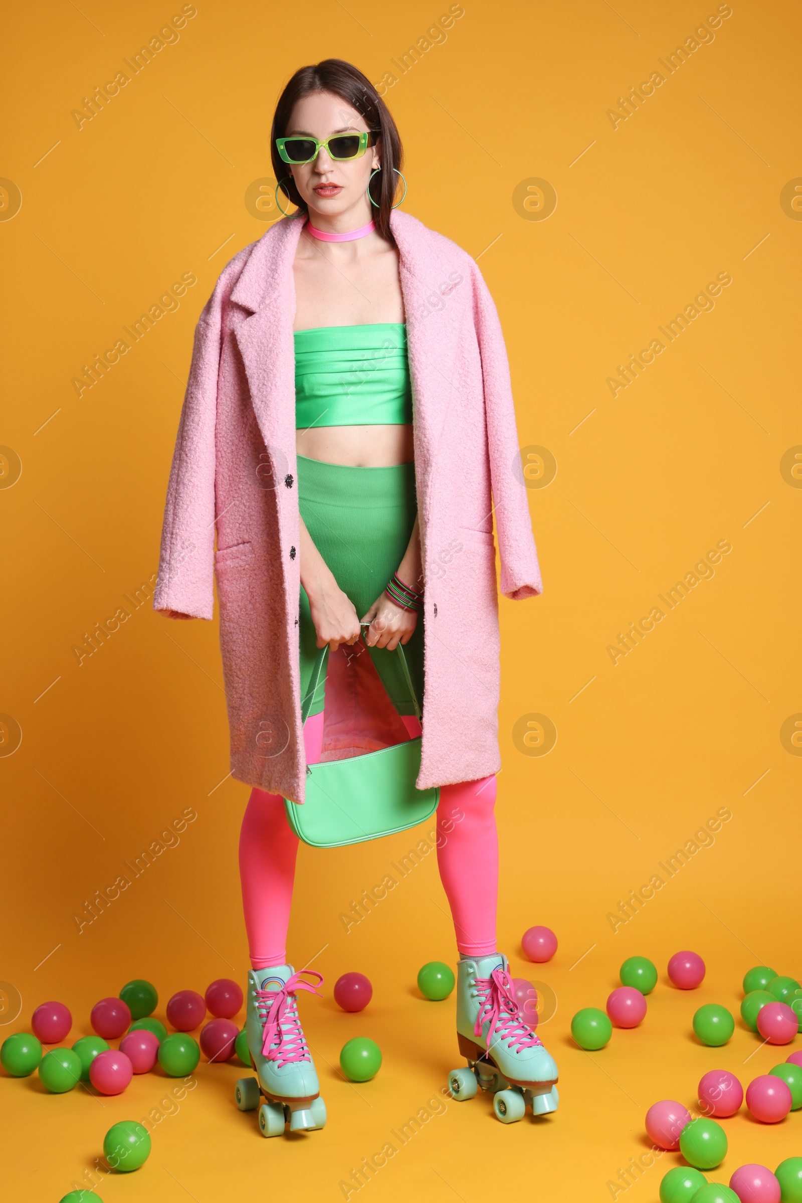 Photo of Stylish woman with retro roller skates and colorful balls on orange background