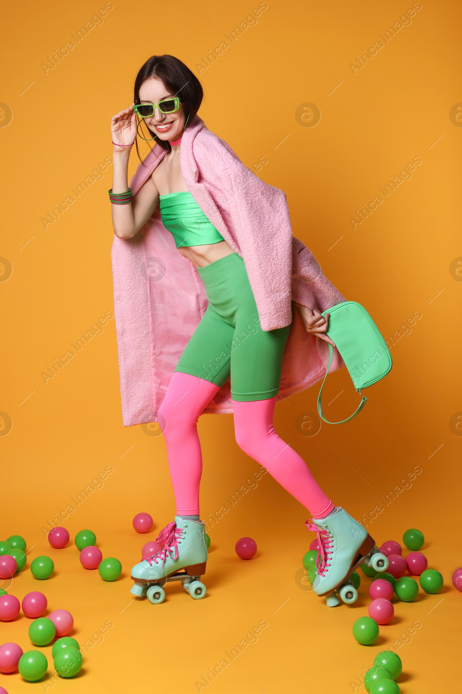 Photo of Stylish woman with retro roller skates and colorful balls on orange background