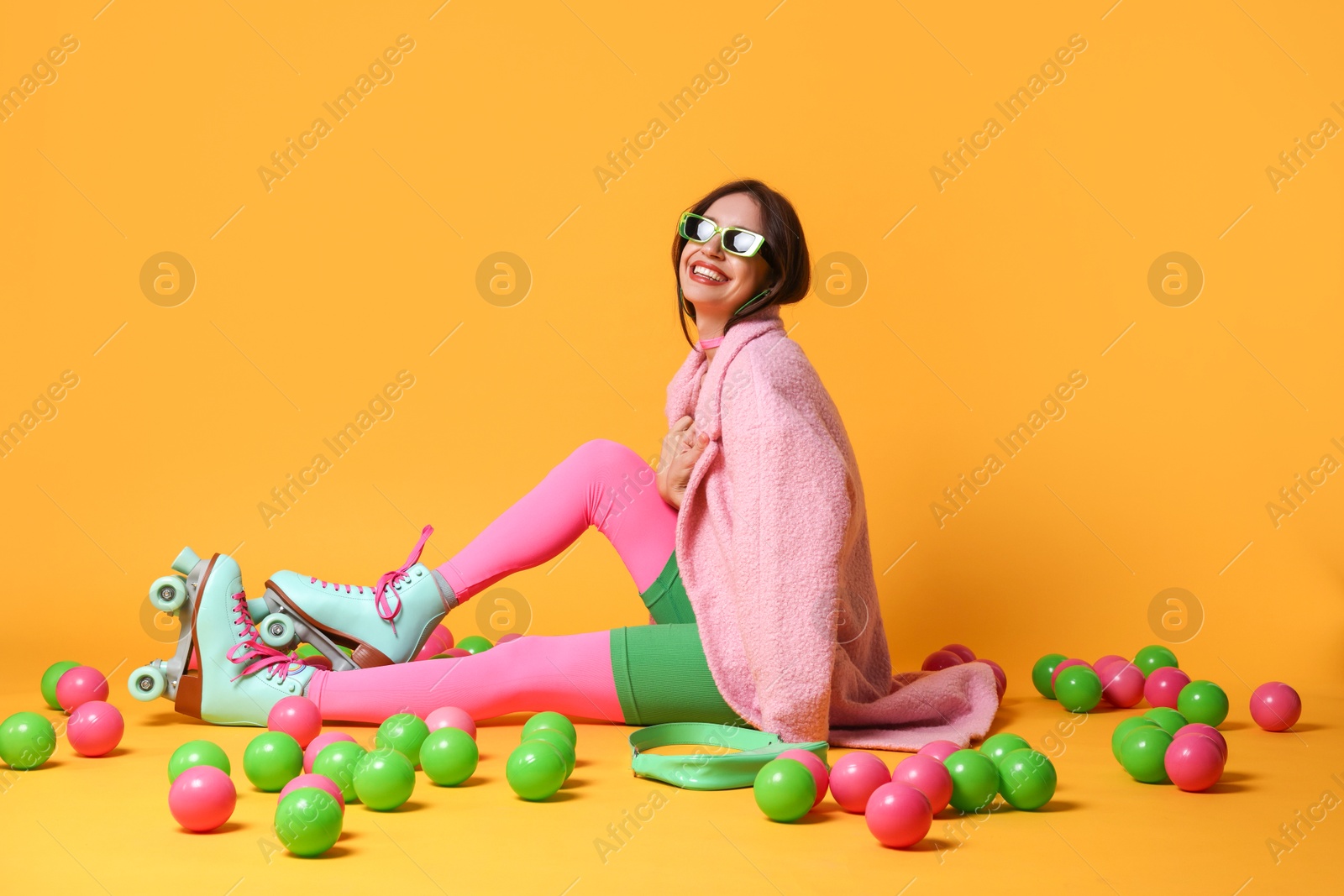 Photo of Stylish woman with retro roller skates and colorful balls on orange background