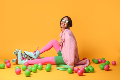 Photo of Stylish woman with retro roller skates and colorful balls on orange background