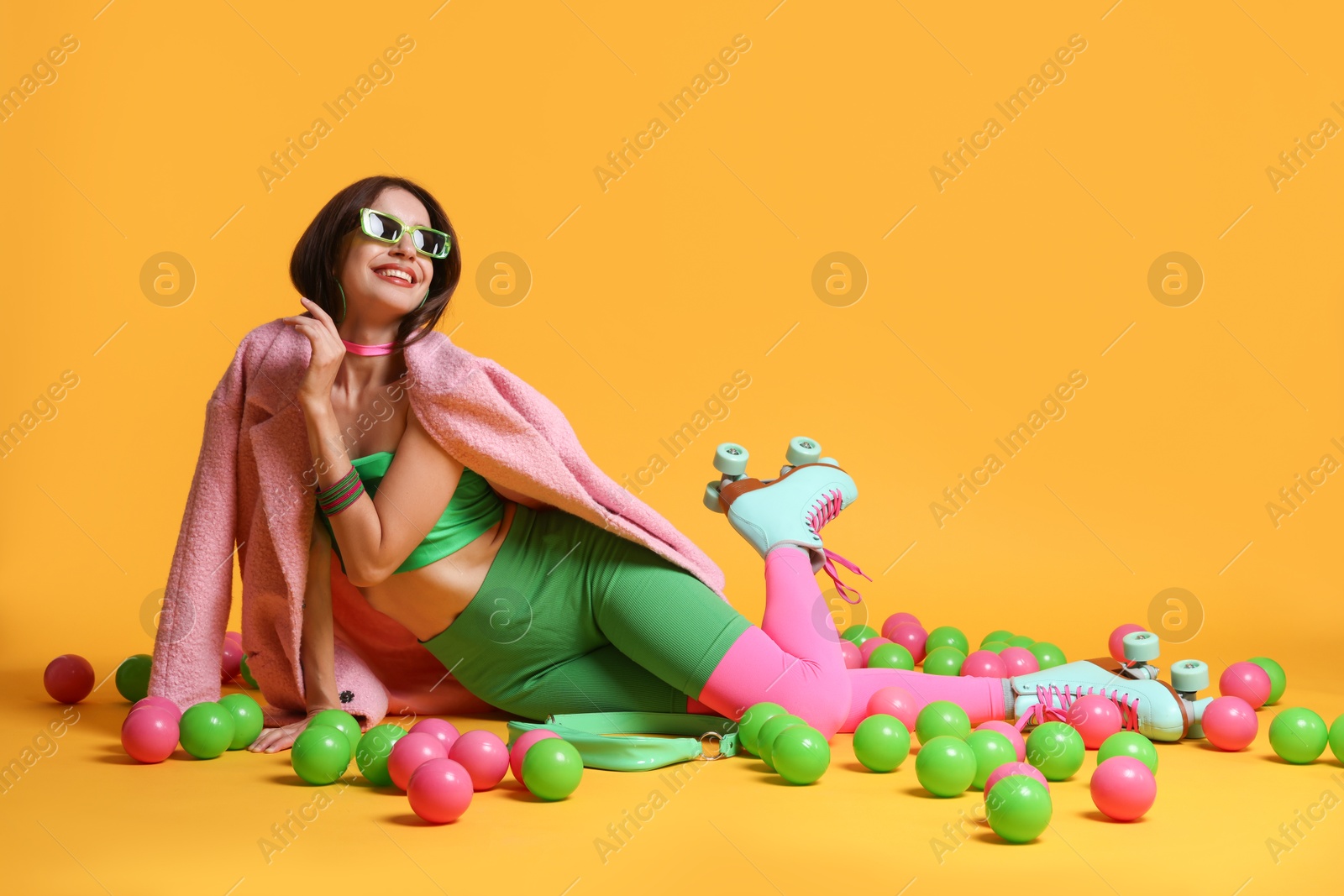 Photo of Stylish woman with retro roller skates and colorful balls on orange background. Space for text