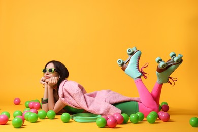 Photo of Stylish woman with retro roller skates and colorful balls on orange background