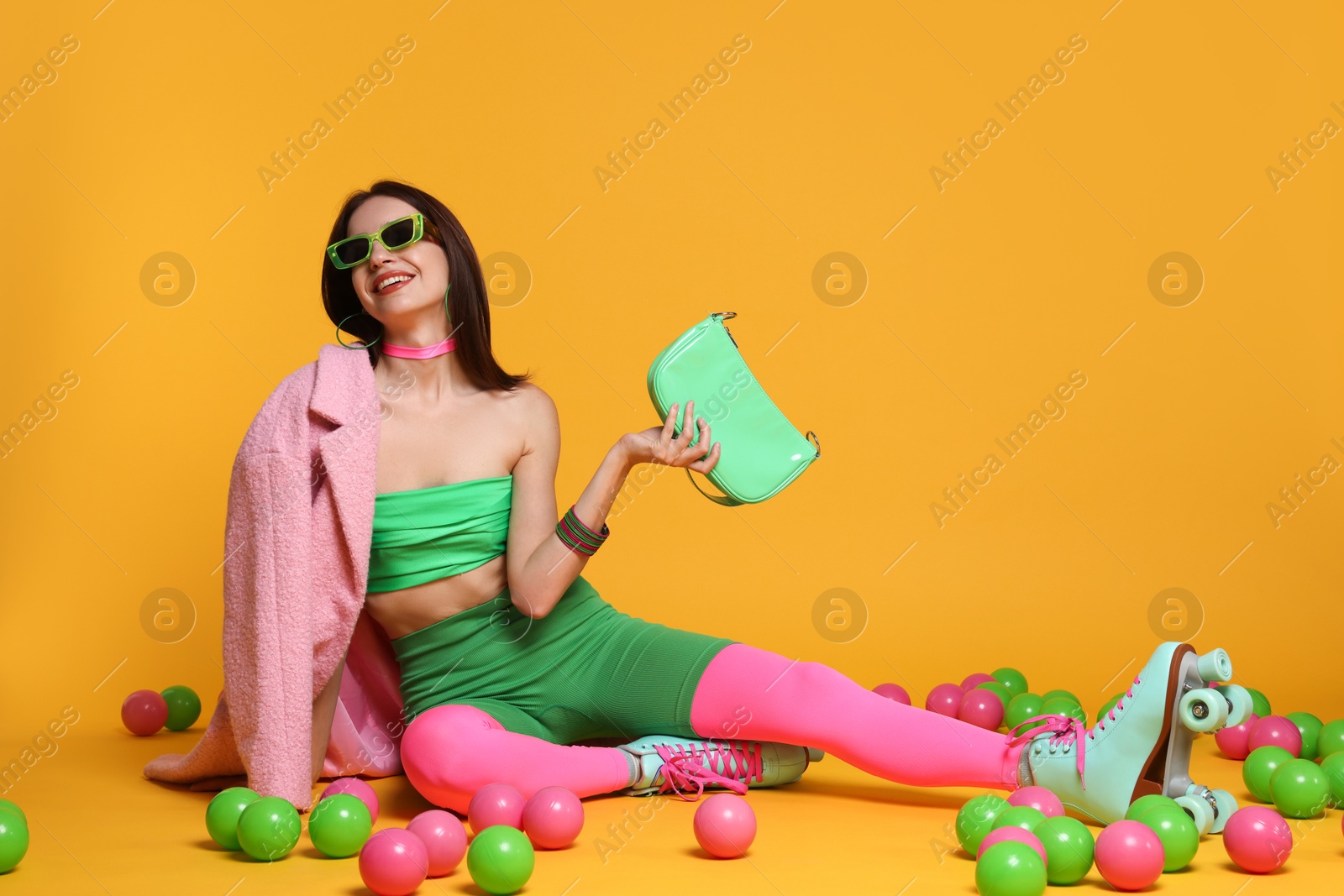 Photo of Stylish woman with retro roller skates and colorful balls on orange background. Space for text