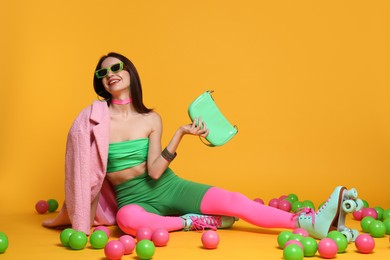 Photo of Stylish woman with retro roller skates and colorful balls on orange background. Space for text