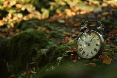 Photo of Alarm clock on fallen dry leaves outdoors, closeup. Space for text