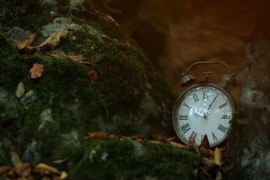 Photo of Alarm clock on fallen dry leaves outdoors, closeup. Space for text