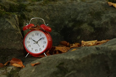 Photo of Alarm clock on fallen dry leaves and stones outdoors, closeup. Space for text