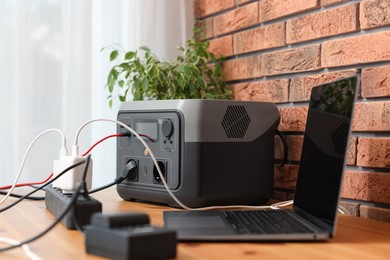 Laptop charging from portable power station on wooden desk indoors