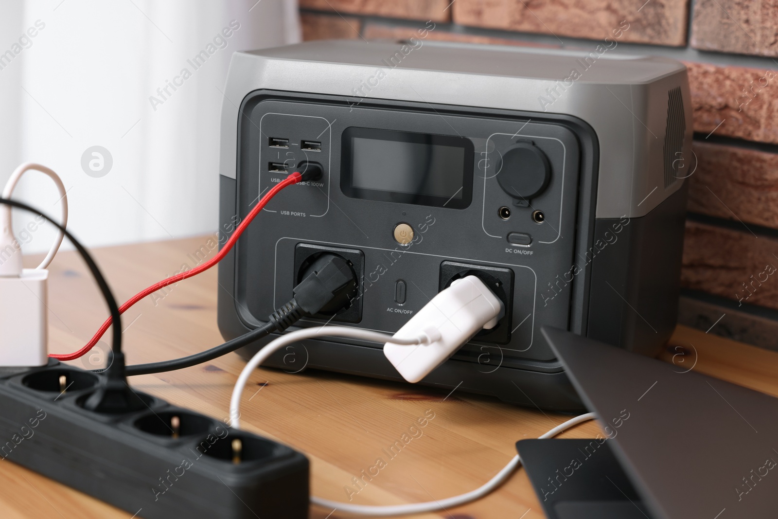 Photo of Laptop charging from portable power station on wooden desk indoors