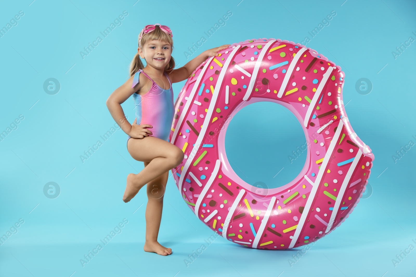 Photo of Cute little girl in beachwear with diving mask and inflatable ring on light blue background