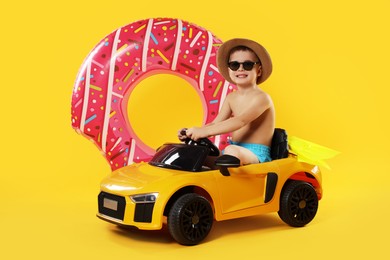 Photo of Cute little boy in beachwear with inflatable ring and toy car on orange background