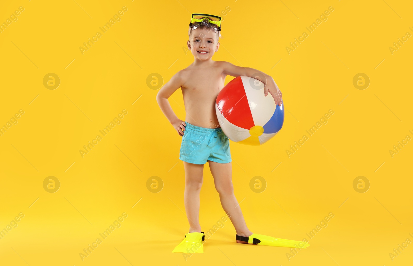 Photo of Cute little boy in beachwear with diving mask and inflatable ball on orange background