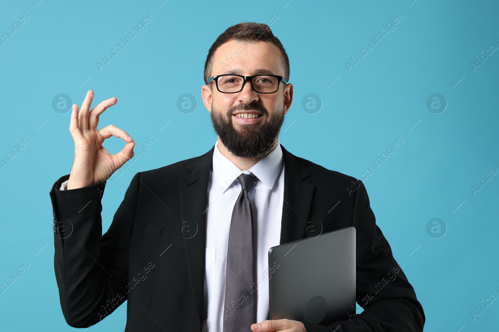 Photo of Smiling businessman with laptop showing okay gesture on light blue background