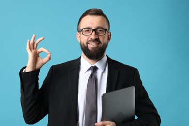 Photo of Smiling businessman with laptop showing okay gesture on light blue background