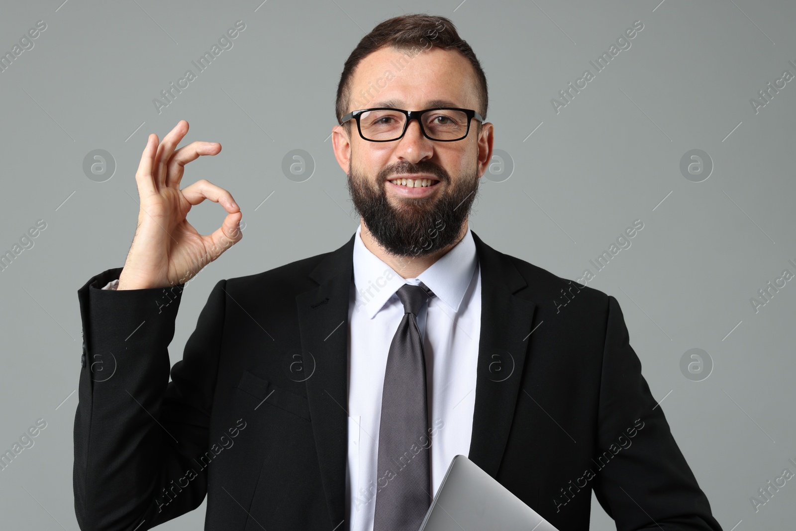 Photo of Smiling businessman showing okay gesture on grey background