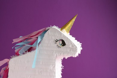 Photo of Bright pinata in shape of unicorn on purple background