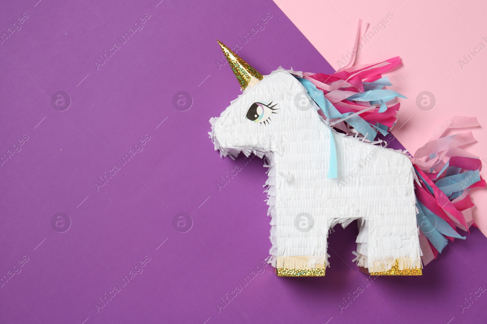 Photo of Bright pinata in shape of unicorn on color background, top view. Space for text