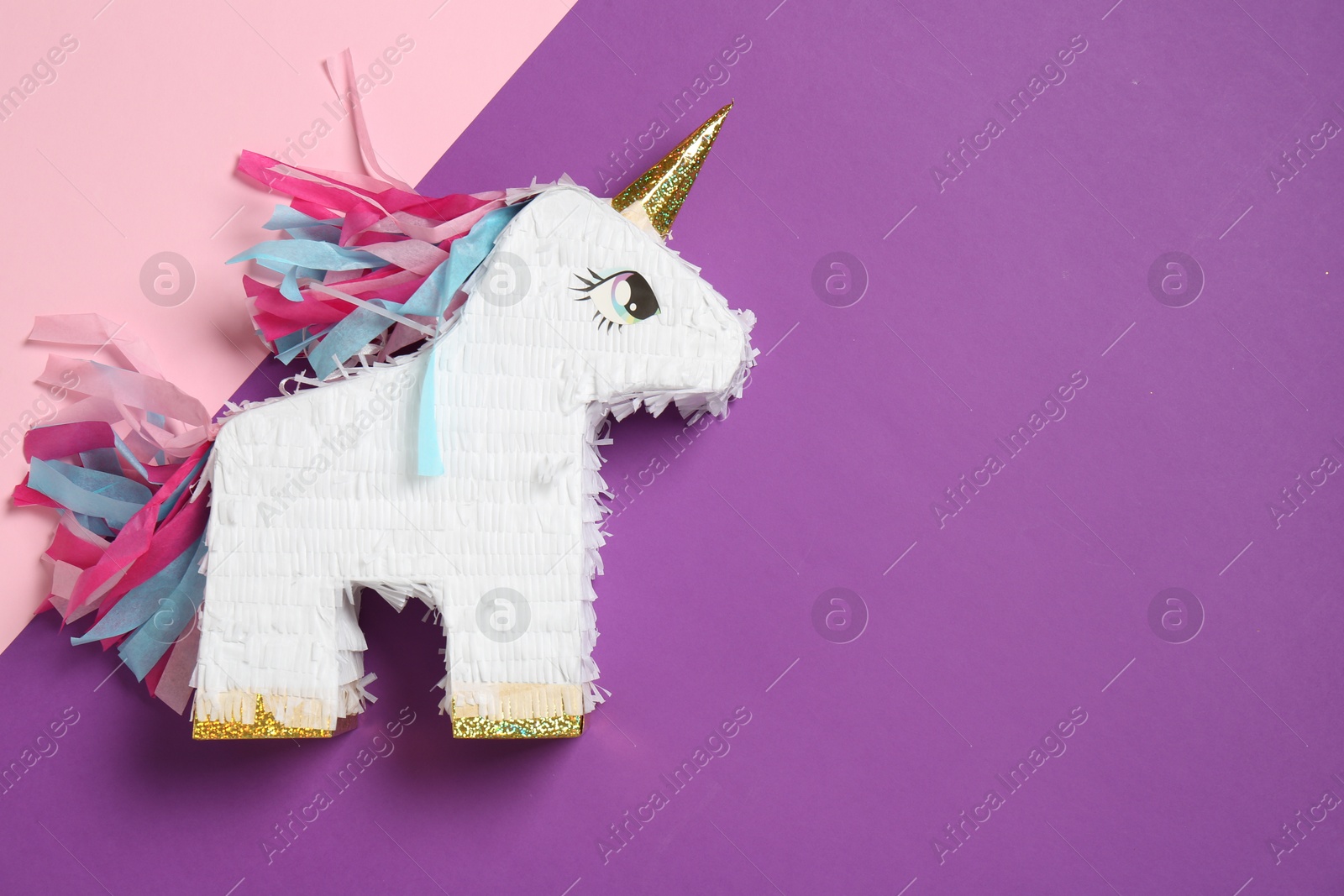 Photo of Bright pinata in shape of unicorn on color background, top view. Space for text