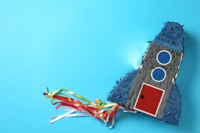 Photo of Bright pinata in shape of spaceship on light blue background, top view. Space for text