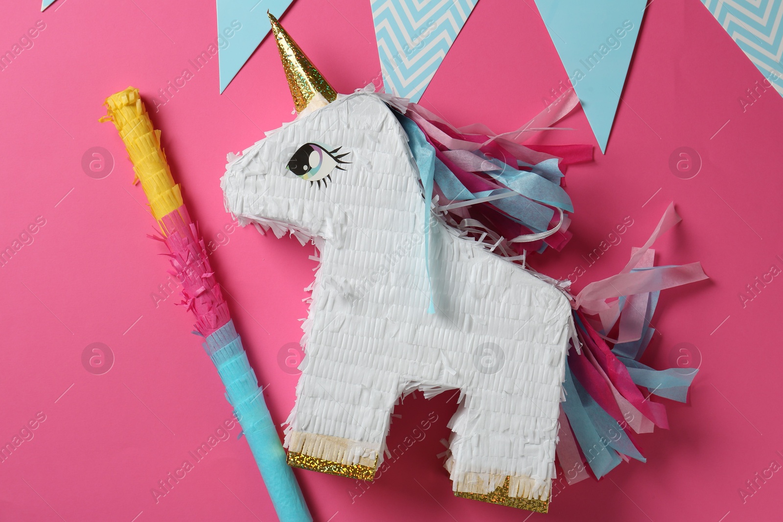 Photo of Bright pinata in shape of unicorn and party accessories on pink background, top view