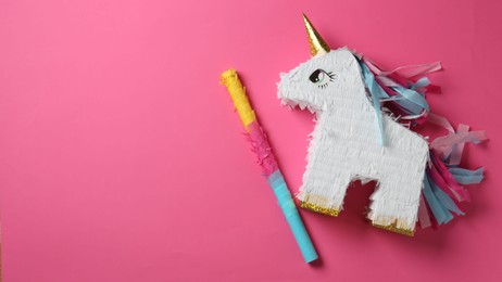 Photo of Bright pinata in shape of unicorn and stick on pink background, top view. Space for text