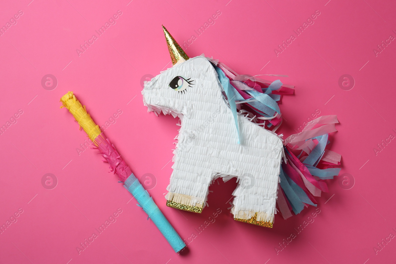 Photo of Bright pinata in shape of unicorn and stick on pink background, top view