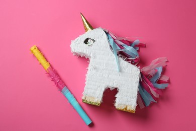 Photo of Bright pinata in shape of unicorn and stick on pink background, top view