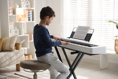 Photo of Little boy playing synthesizer at home. Electronic musical instrument