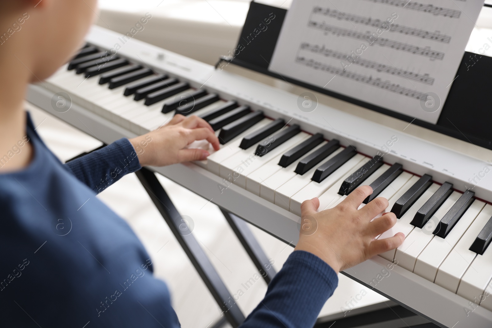 Photo of Boy playing synthesizer indoors, closeup. Electronic musical instrument