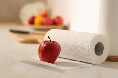 Photo of Roll of paper towels and red apple on white countertop in kitchen, closeup