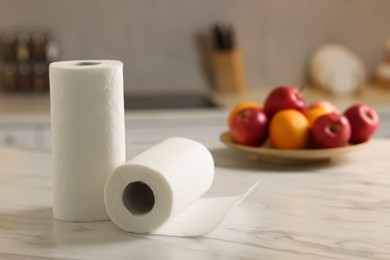 Photo of Rolls of paper towels and fruits on white marble table in kitchen