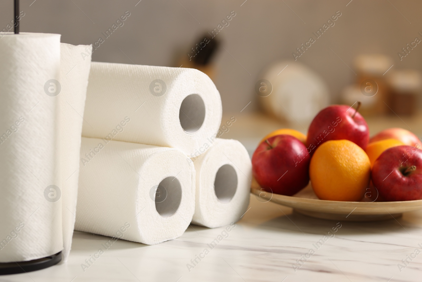 Photo of Rolls of paper towels and fruits on white marble table in kitchen