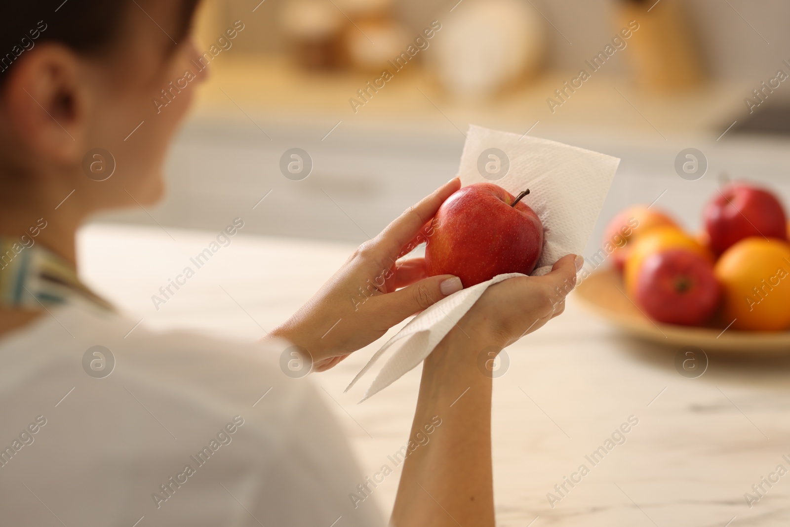 Photo of Woman wiping apple with paper towel in kitchen, closeup